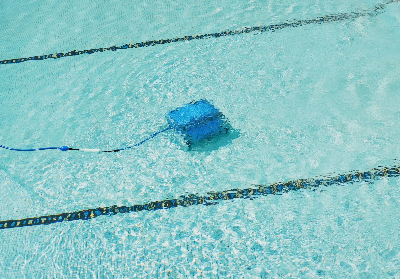 A robotic pool cleaner operating at the bottom of a crystal-clear lap pool with lane dividers visible
