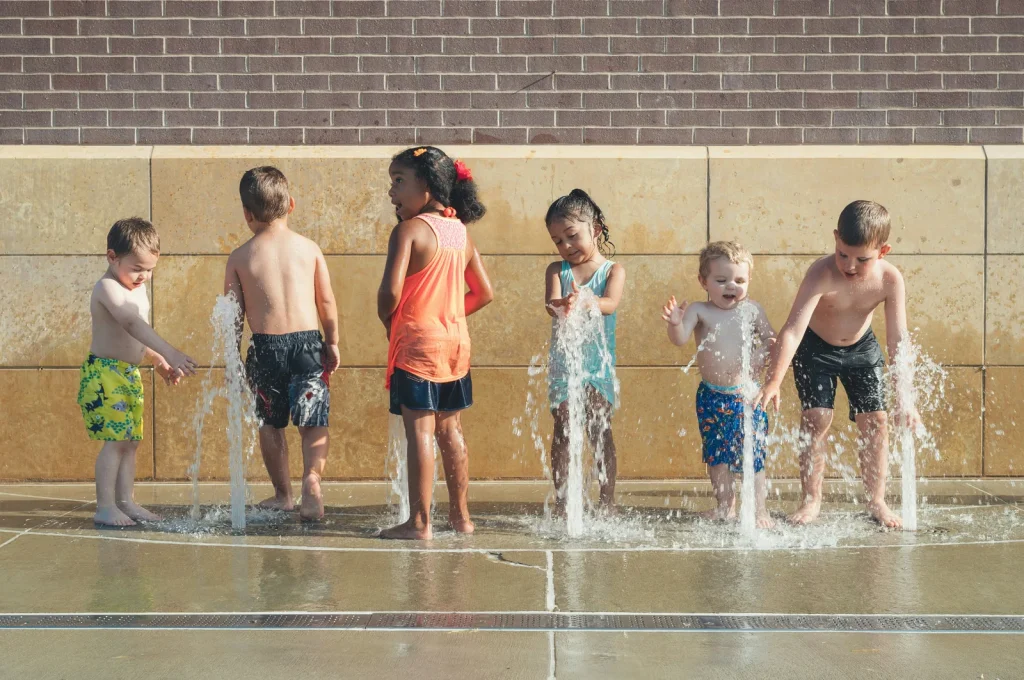 Five children playing at outdoor water fountains and splash pad in summer