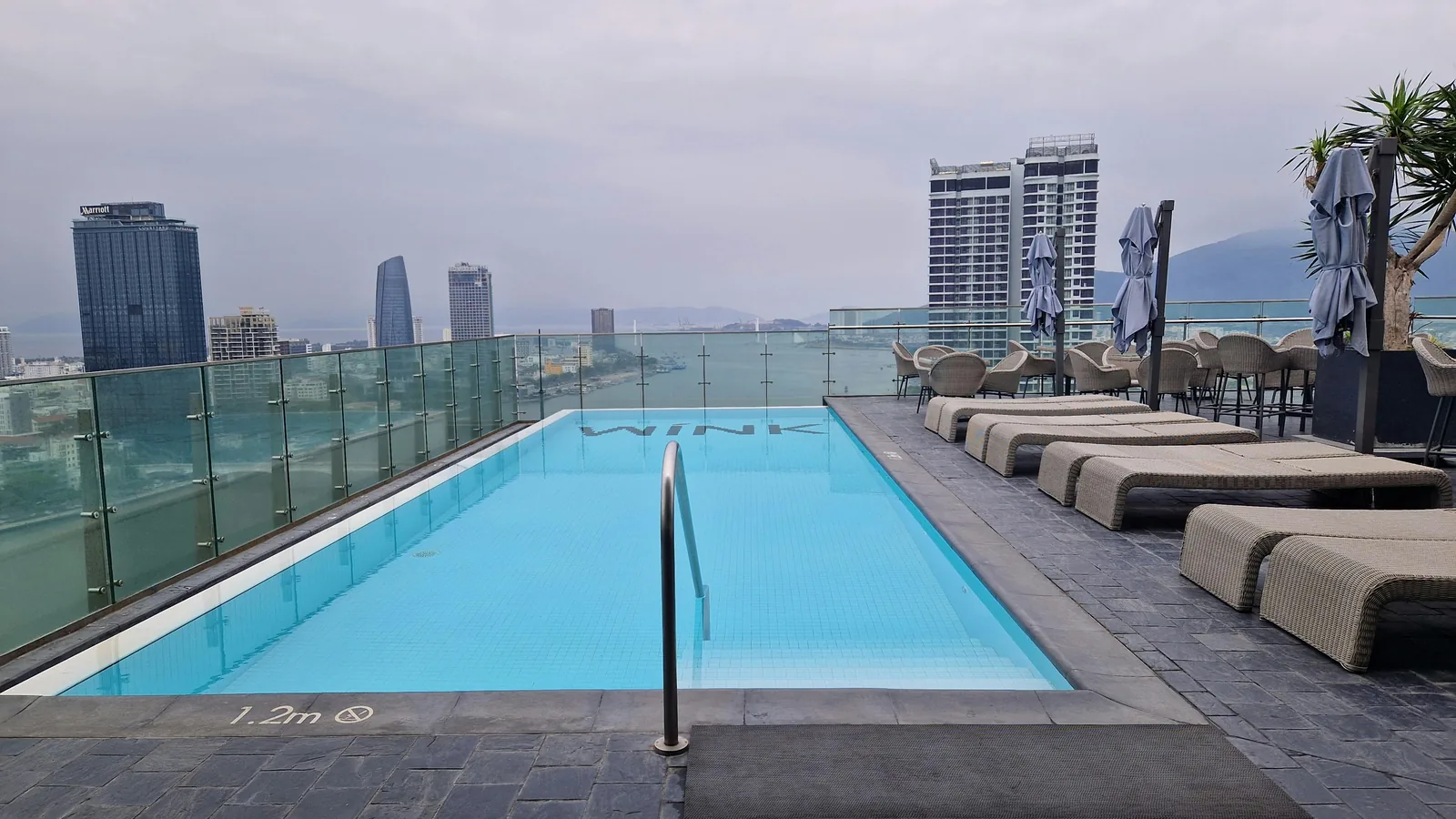 A rooftop hotel pool with clear blue water and sun loungers overlooking a city skyline