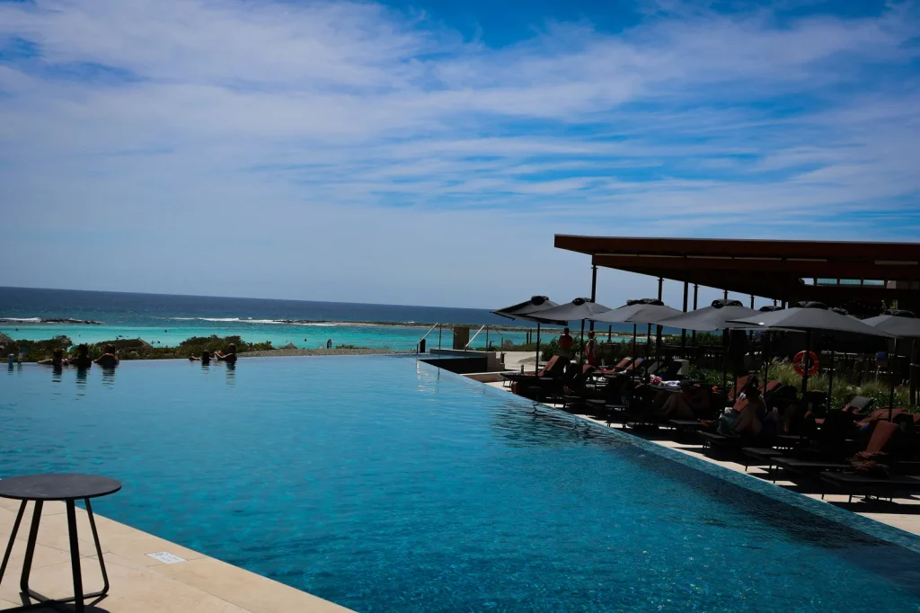 Luxury resort infinity pool with sun loungers overlooking turquoise ocean and blue sky