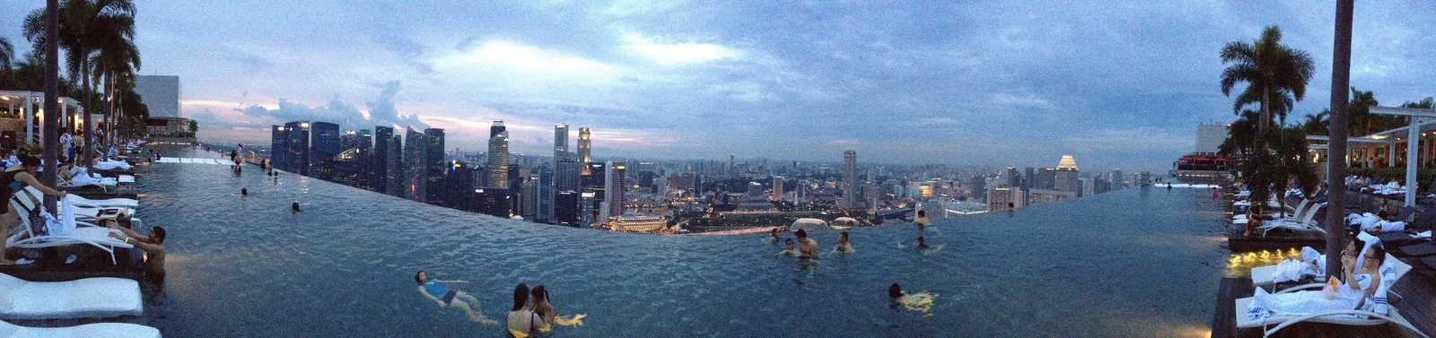 Marina Bay Sands infinity pool with Singapore city skyline at dusk, swimmers visible