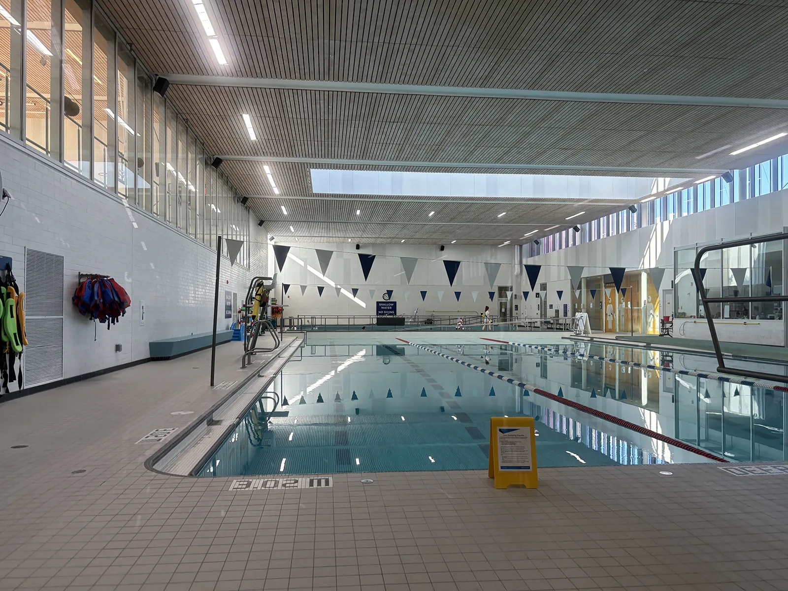 Interior view of a modern community indoor swimming pool with lane ropes, life-saving equipment on the wall, and a glass roof, representing the community leisure centre facilities including Formby Pool Trust near Liverpool
