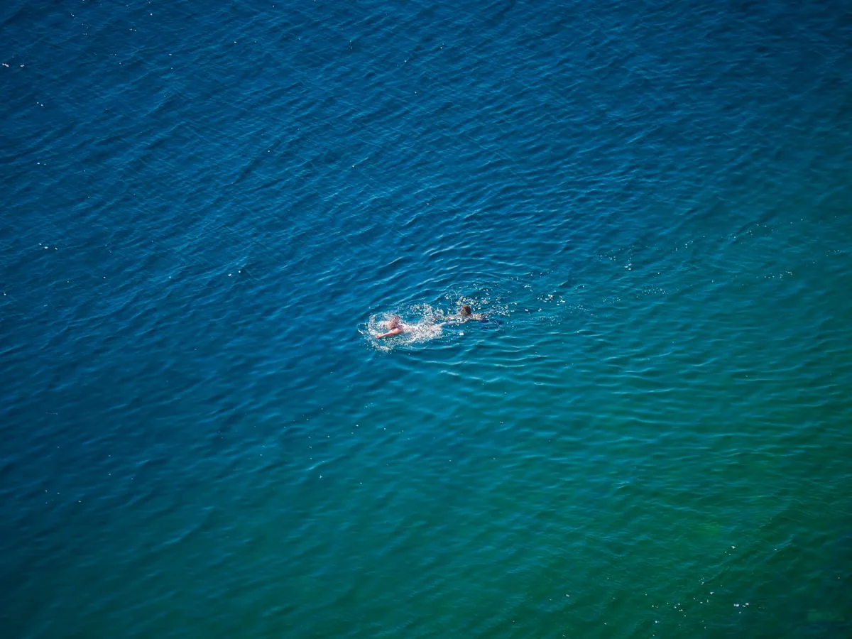 Aerial view of a lone swimmer in deep turquoise-blue open water, representing open water swimming at Liverpool Watersports Centre at Queens Dock and on the River Mersey