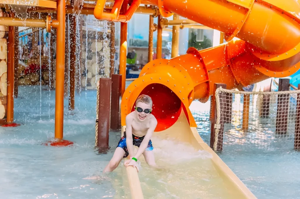 Young child laughing as he exits an orange tube water slide at an indoor waterpark