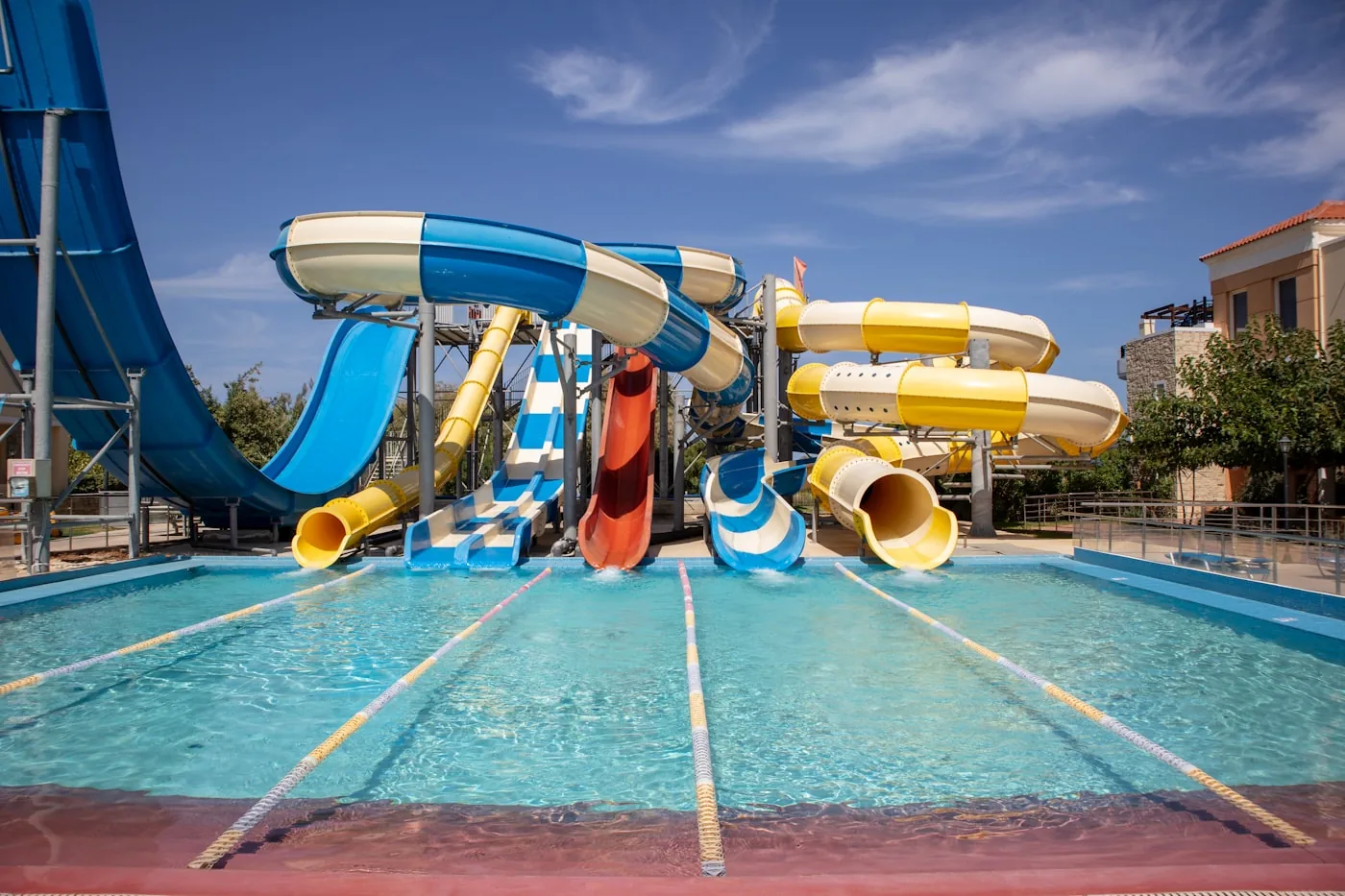 Multiple colourful water slides — blue, yellow and red — at an outdoor water park descending into a pool