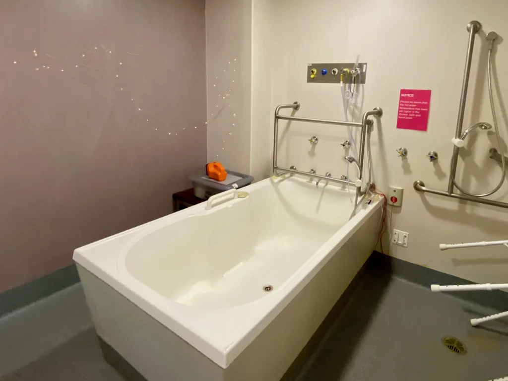 A large white birth pool in a hospital birth suite with grab rails and star-effect ceiling, representing an NHS birthing pool room
