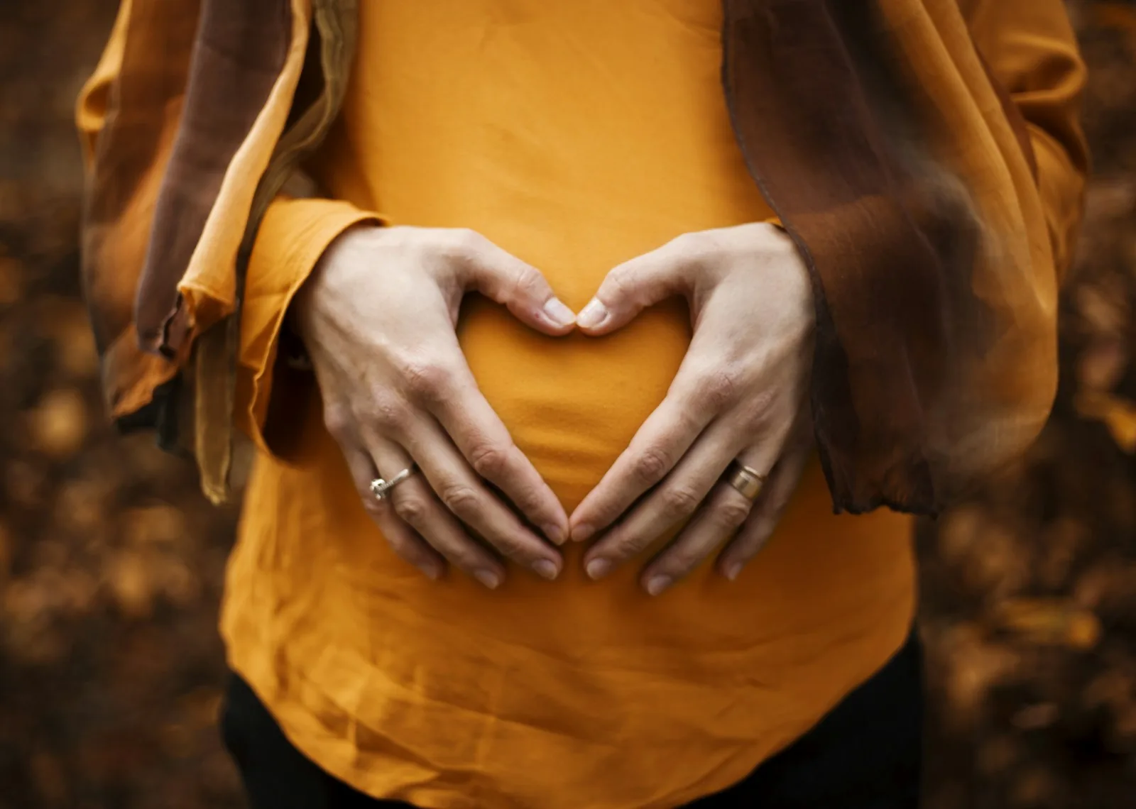 Close-up of pregnant woman making a heart shape with her hands on her baby bump, representing the preparation for a home water birth