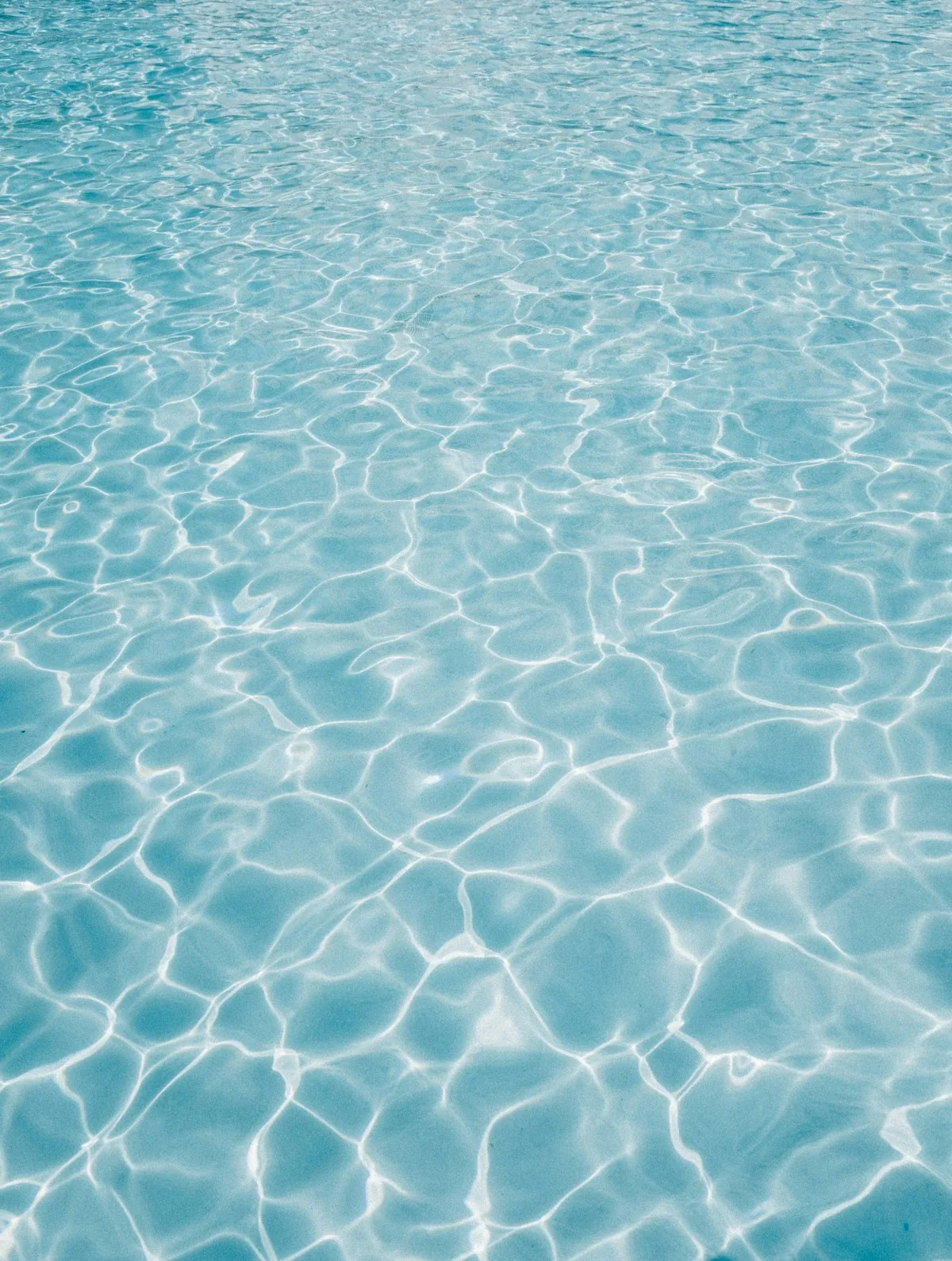Close-up of clear blue chlorinated swimming pool water with light ripples on the surface, representing the question of whether pool water can cause or transmit thrush (Candida yeast infection)