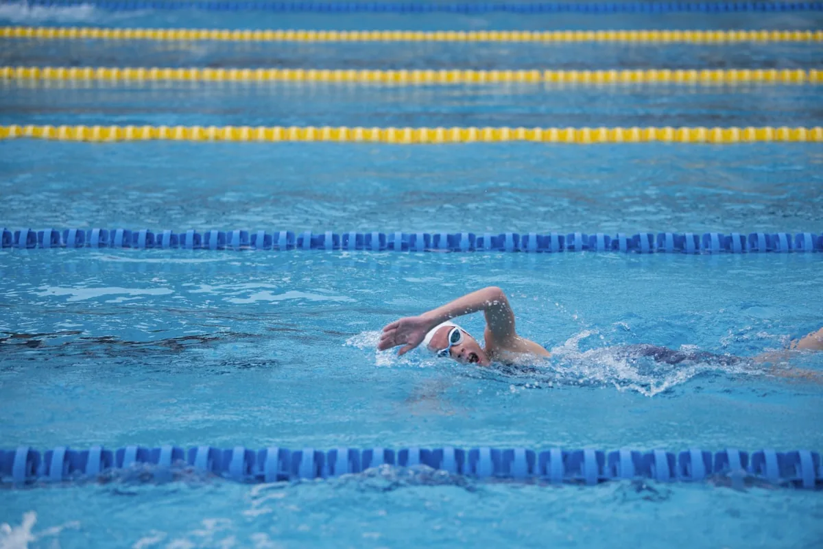 A swimmer wearing a white cap and goggles performing front crawl in a blue lane pool, representing the question of whether it is safe to swim with an active thrush infection