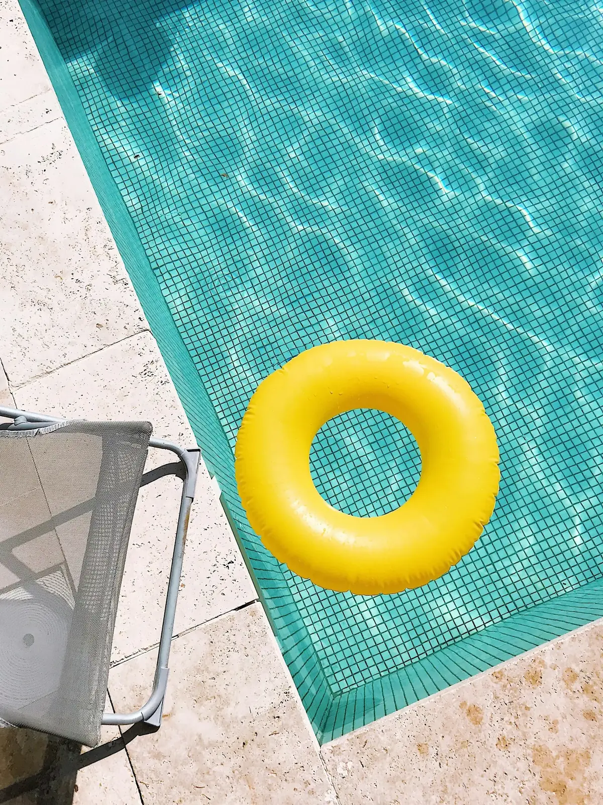 Private outdoor pool with green mosaic tiles and a yellow inflatable ring, representing a residential pool comparing saltwater and chlorine treatment options