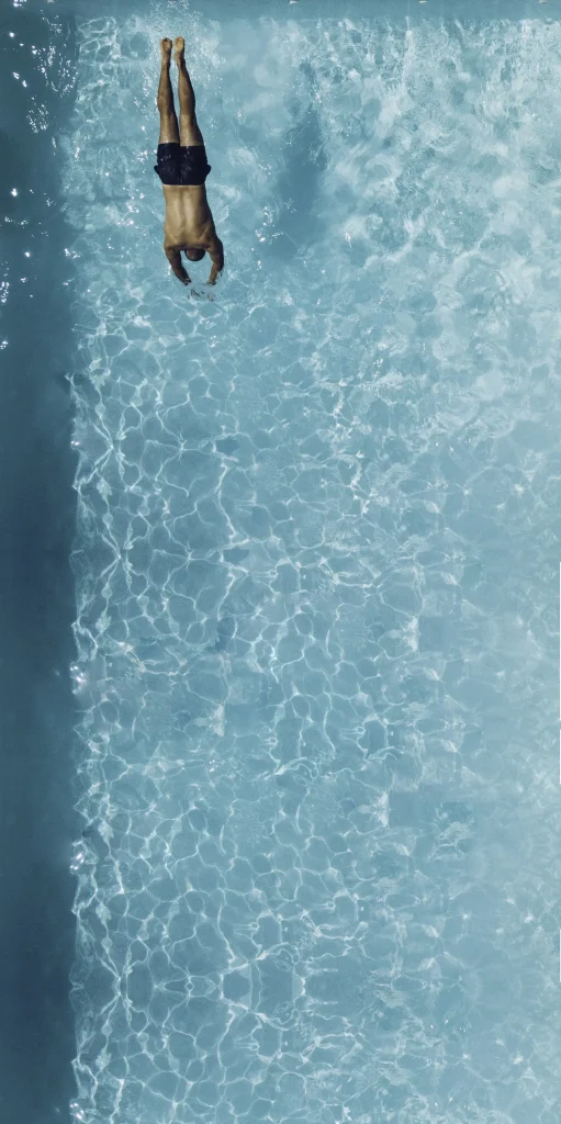 Aerial view of a swimmer diving into clear blue pool water, representing the swimming experience in saltwater pools
