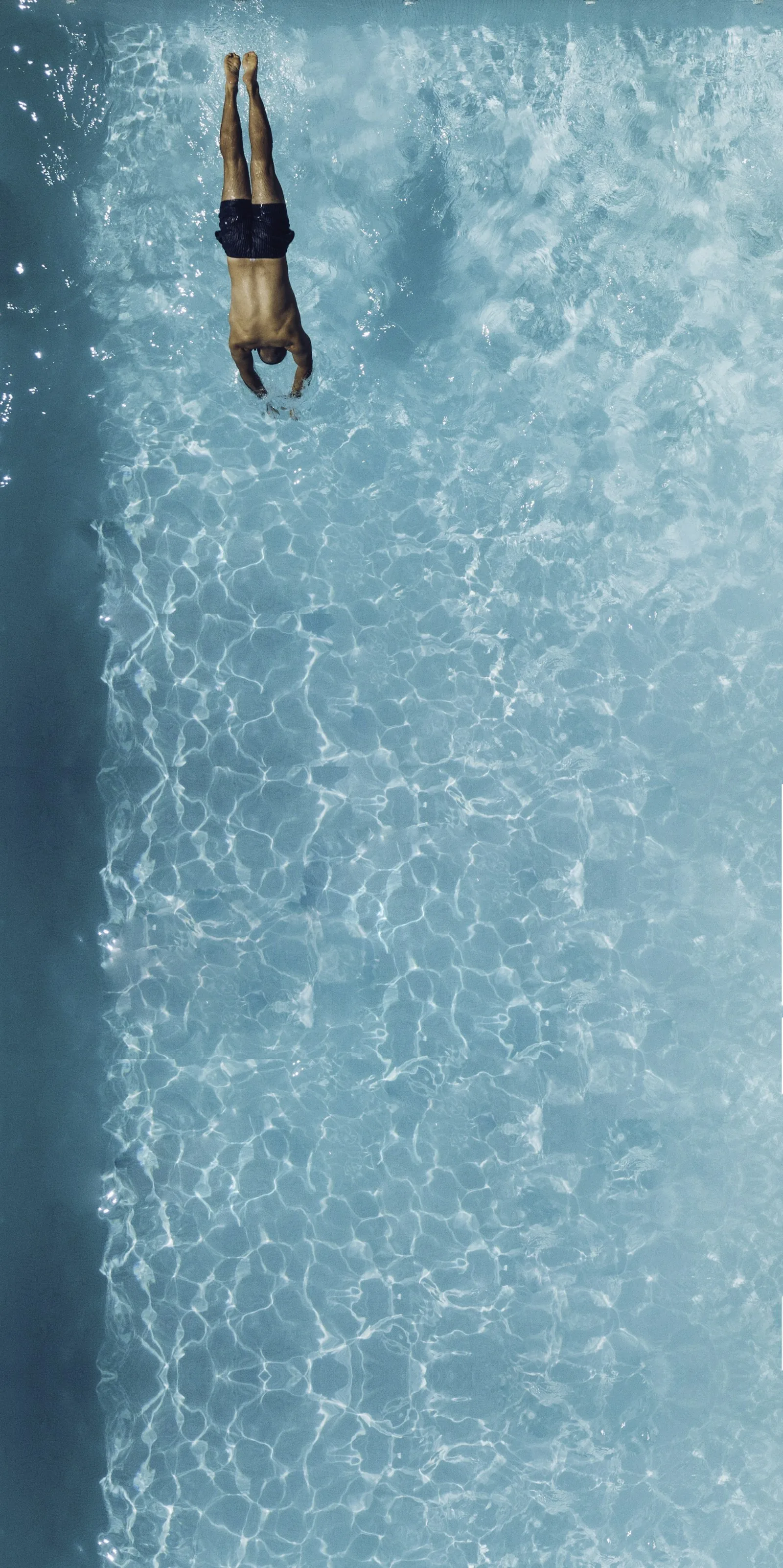 Aerial view of a swimmer diving into clear blue pool water, representing the swimming experience in saltwater pools