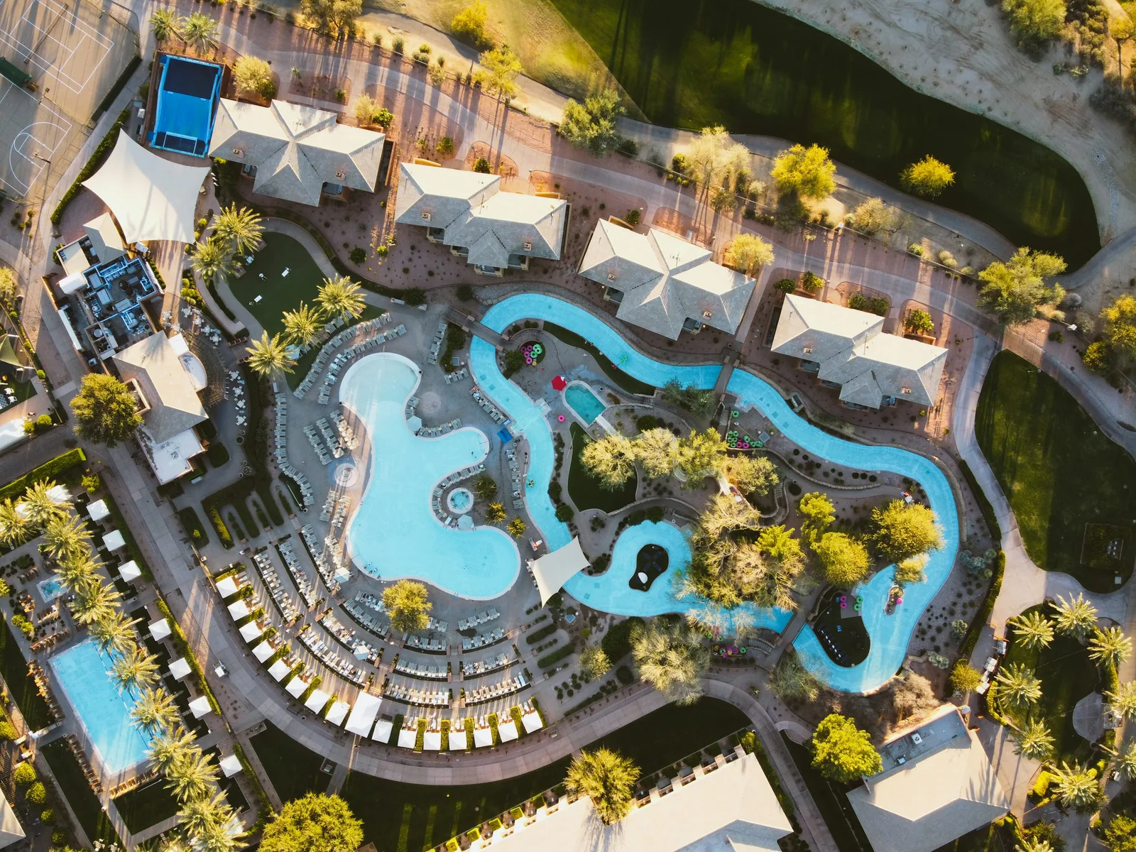 Aerial view of a large resort swimming pool complex surrounded by palm trees and sun loungers