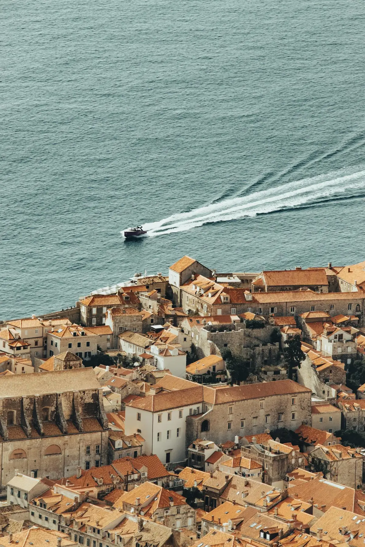Aerial panoramic view of Dubrovnik Croatia's Old Town with orange rooftops and the deep blue Adriatic Sea visible beyond the historic city walls, representing the Dubrovnik coastal hotel setting for pool hotels