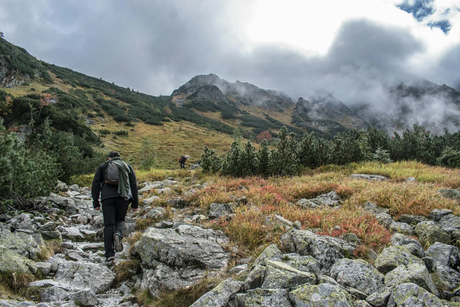 Walker on a rocky fell trail beneath misty mountain scenery similar to the Wasdale Fairy Pools walk