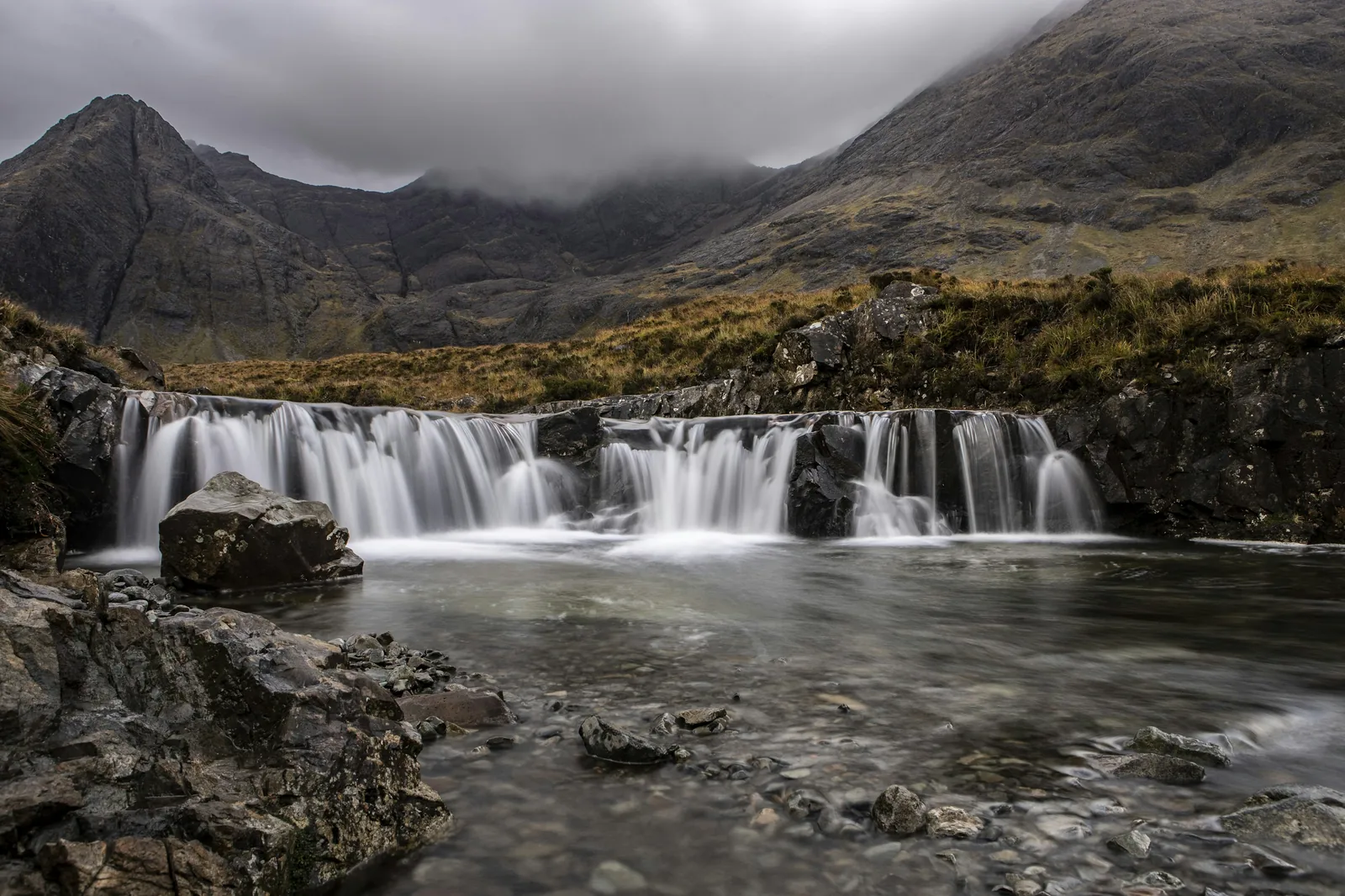 Crystal clear turquoise water in a rocky mountain pool surrounded by highland landscape with dramatic sky representing the famous Fairy Pools of the Isle of Skye Scotland
