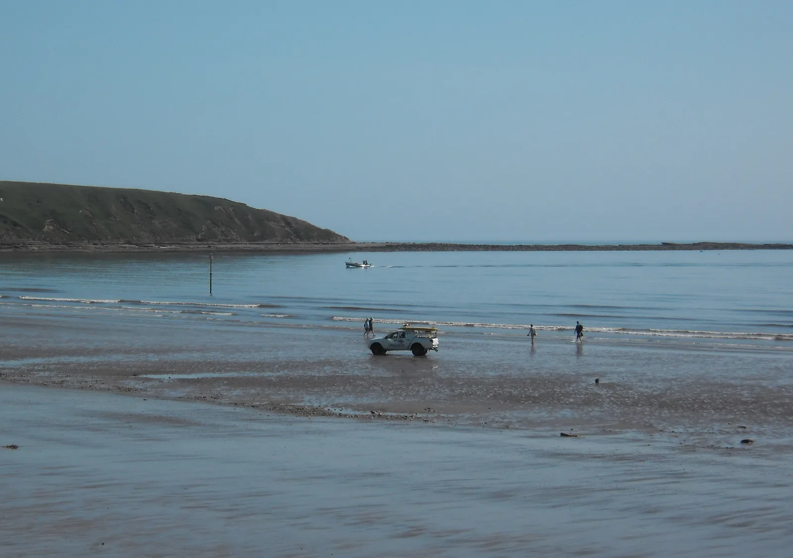 Filey Sands beach at low tide with Filey Brigg headland visible in the background, people paddling and a beach vehicle on the sand, Yorkshire coast