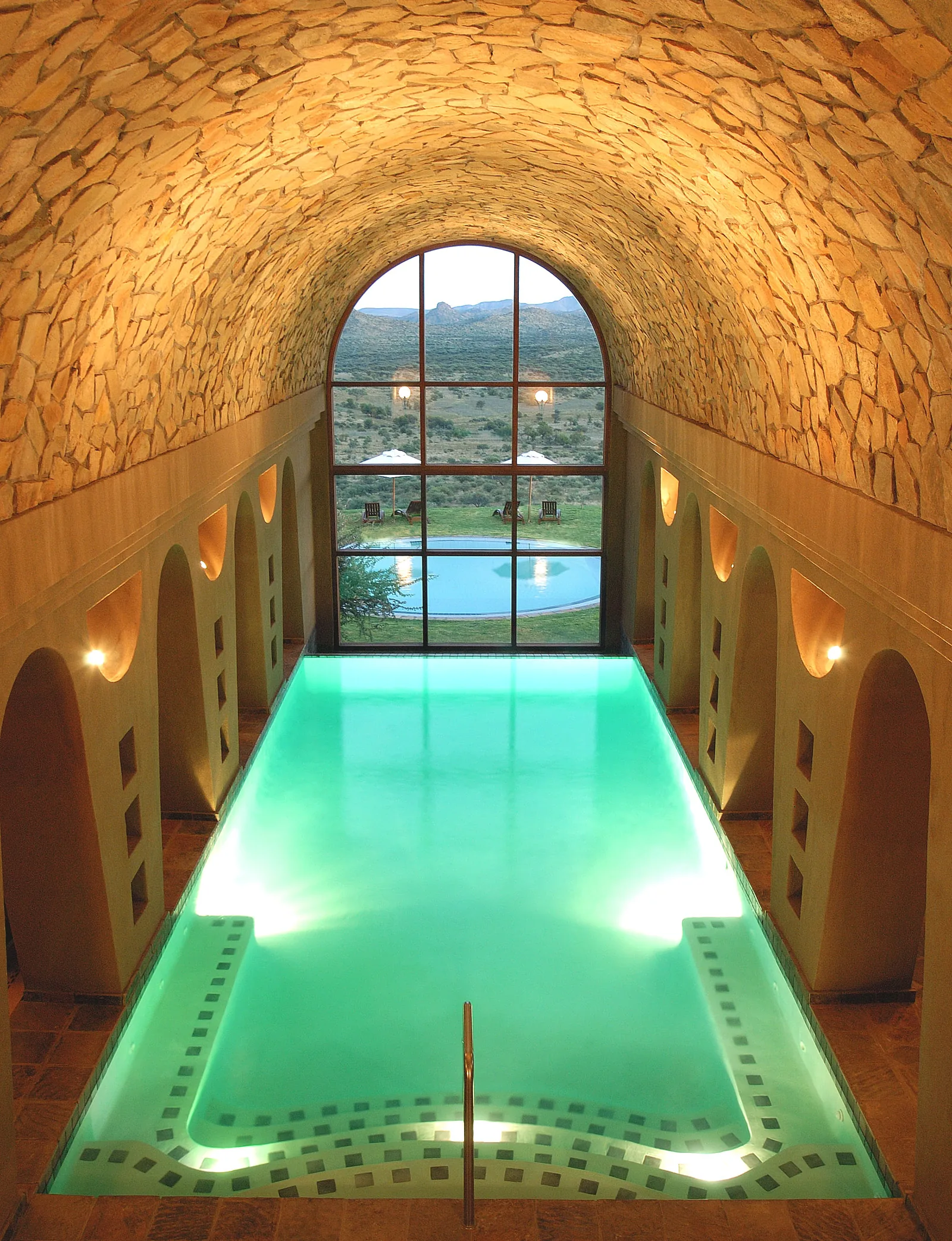 Luxury indoor heated swimming pool under stone barrel-vault ceiling with arched window