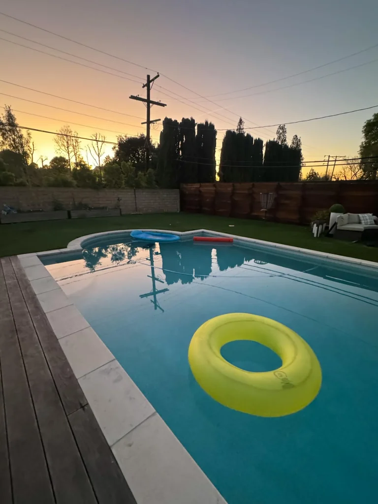 A backyard inground swimming pool at sunset with pool floats and wooden decking — residential pool heating with air-source heat pumps
