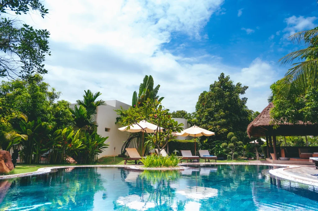 An outdoor resort swimming pool surrounded by lush tropical greenery with sun loungers and parasols