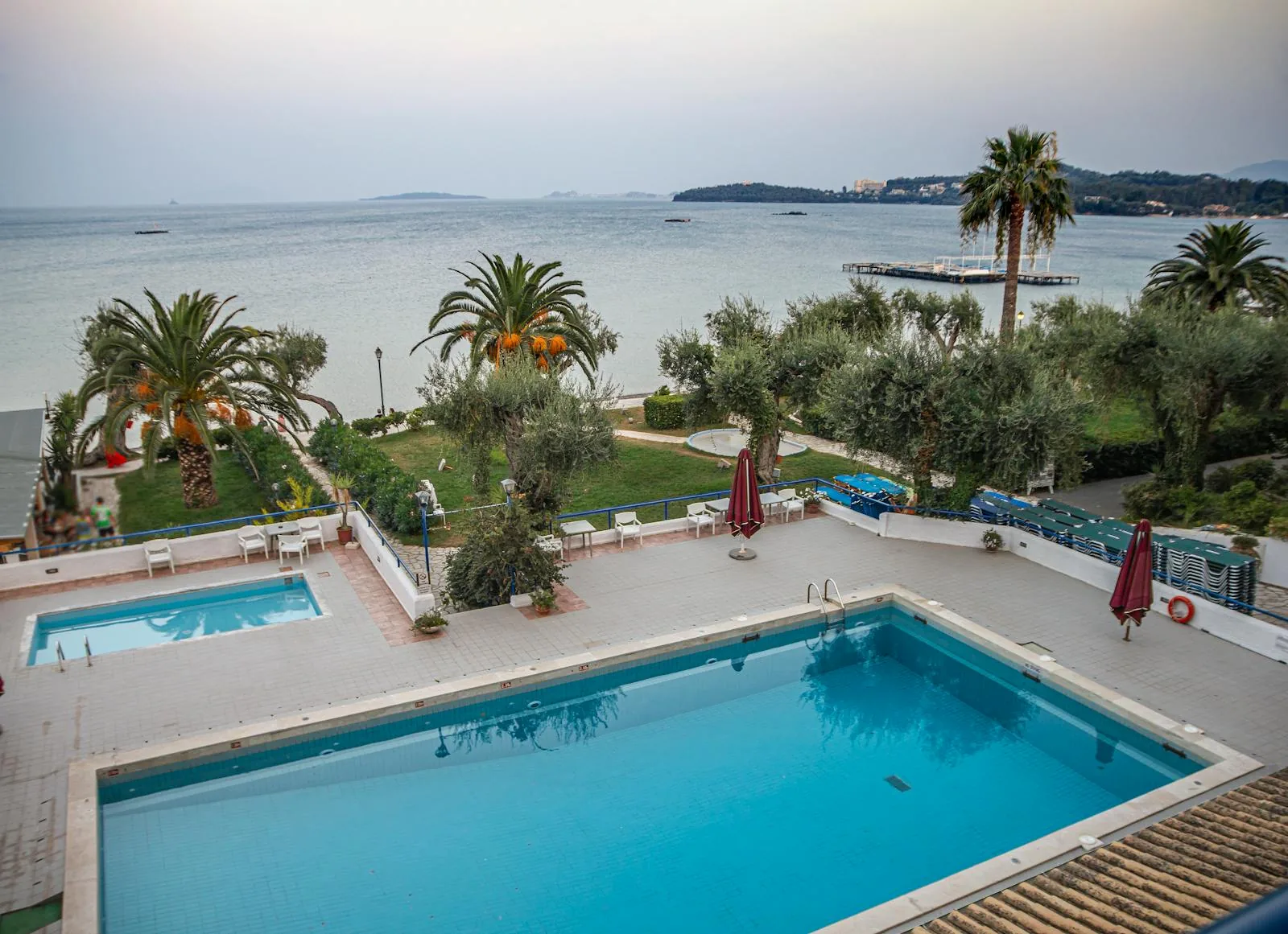 An outdoor resort swimming pool with sun loungers and palm trees in a Greek island setting under a clear blue sky representing swim-up pool hotels in Corfu Zakynthos and Halkidiki