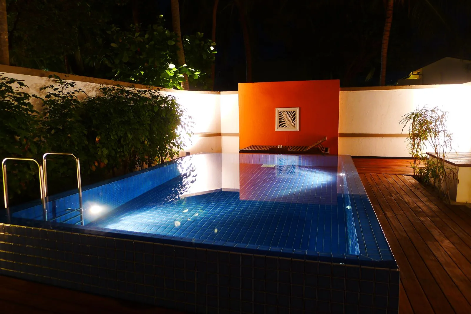 Illuminated private pool at a hotel villa at night with wooden deck and tropical garden