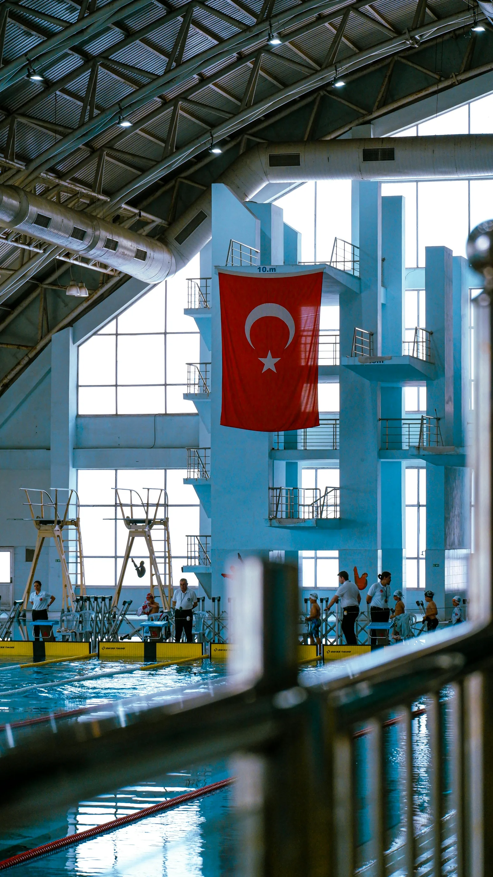An indoor competition swimming pool with a diving platform tower and clear deep blue water viewed from the pool deck representing the depth requirements and safety considerations for competitive diving pools