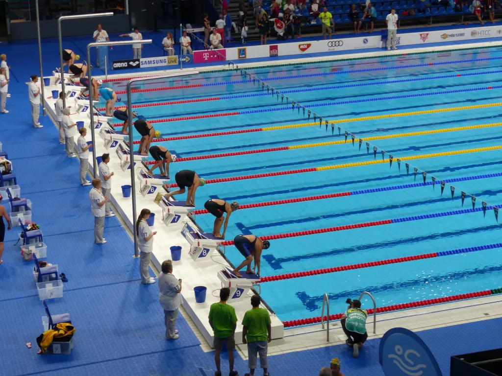 Competitive swimmers at starting blocks of an indoor competition swimming pool with numbered lanes