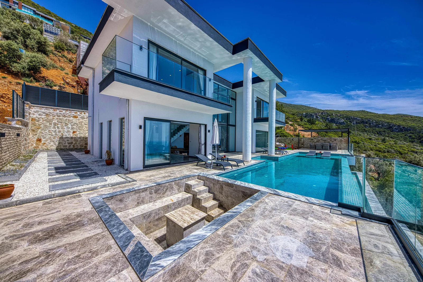 A luxury residential infinity pool with a stone terrace overlooking a valley landscape