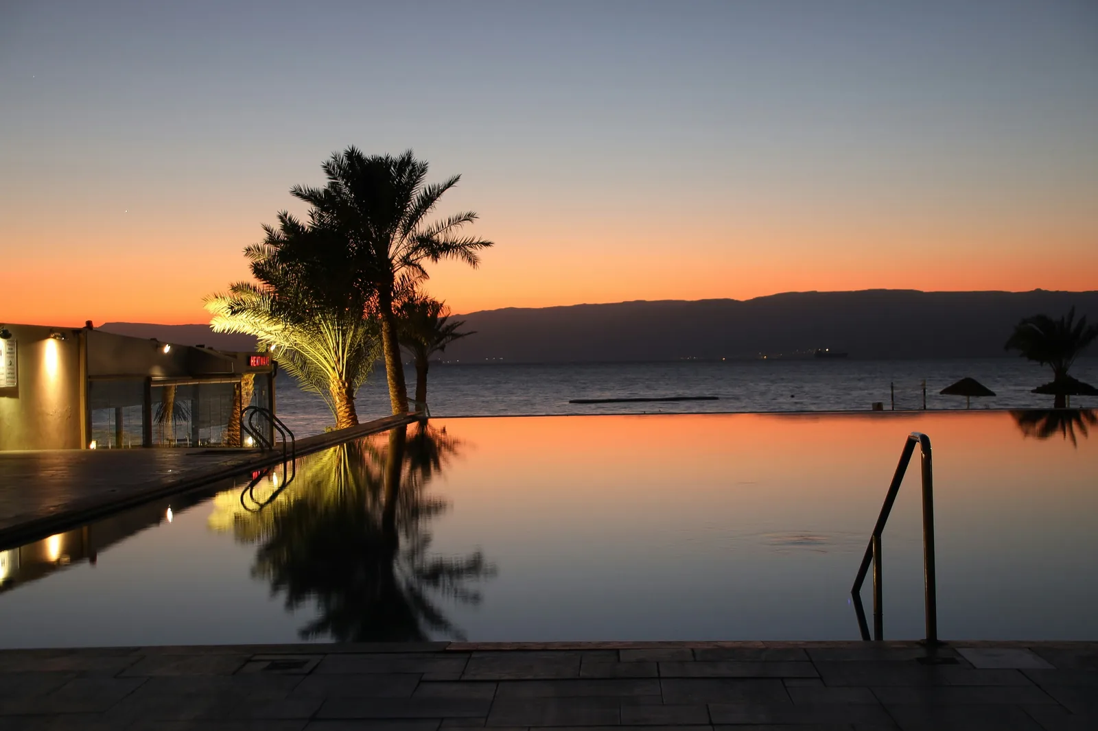 An infinity pool with a vanishing edge appearing to merge with the ocean horizon at a luxury resort at sunset