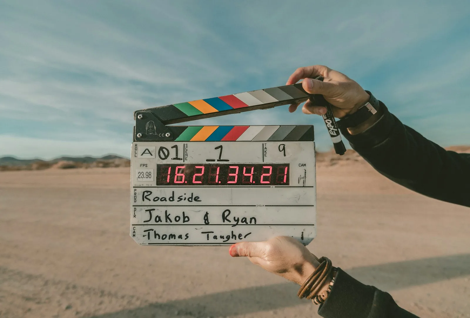 A digital film production clapperboard with multicoloured stripes held up against a clear blue sky, showing production details, representing the Twickenham Studios film and television production planned for the redeveloped Littlewoods Pools building in Liverpool