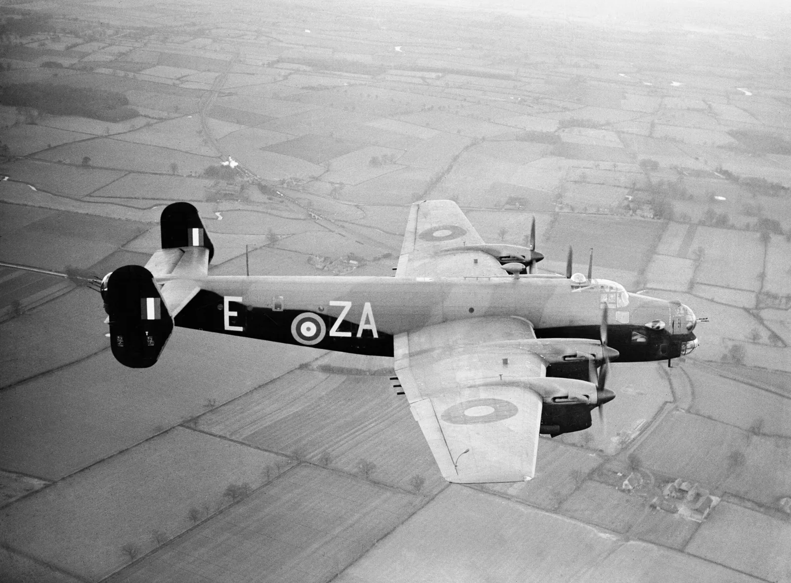 Black and white aerial photograph of a Handley Page Halifax Mk II heavy bomber of No. 10 Squadron RAF marked ZA-E in flight over patchwork English farmland in December 1941, representing the Halifax bombers whose floors were manufactured at the Littlewoods Pools building during the Second World War