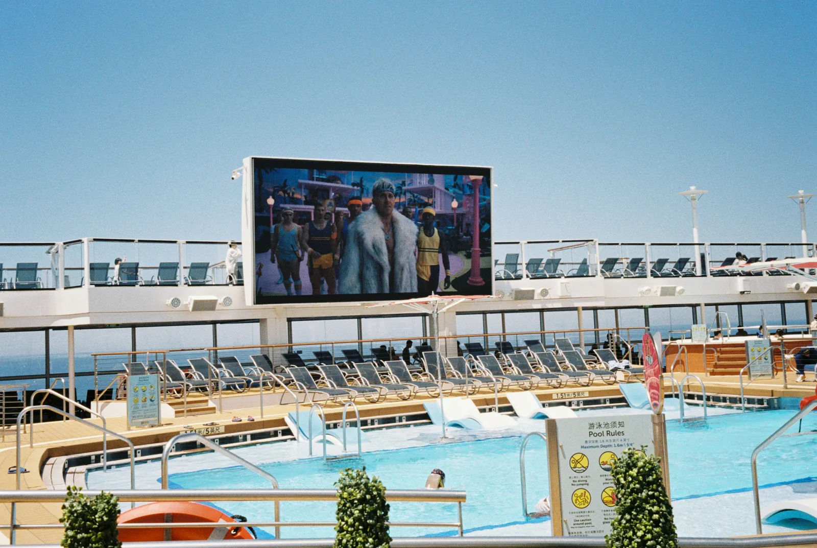 Cruise ship lido deck pool with large screen, sun loungers and blue sky