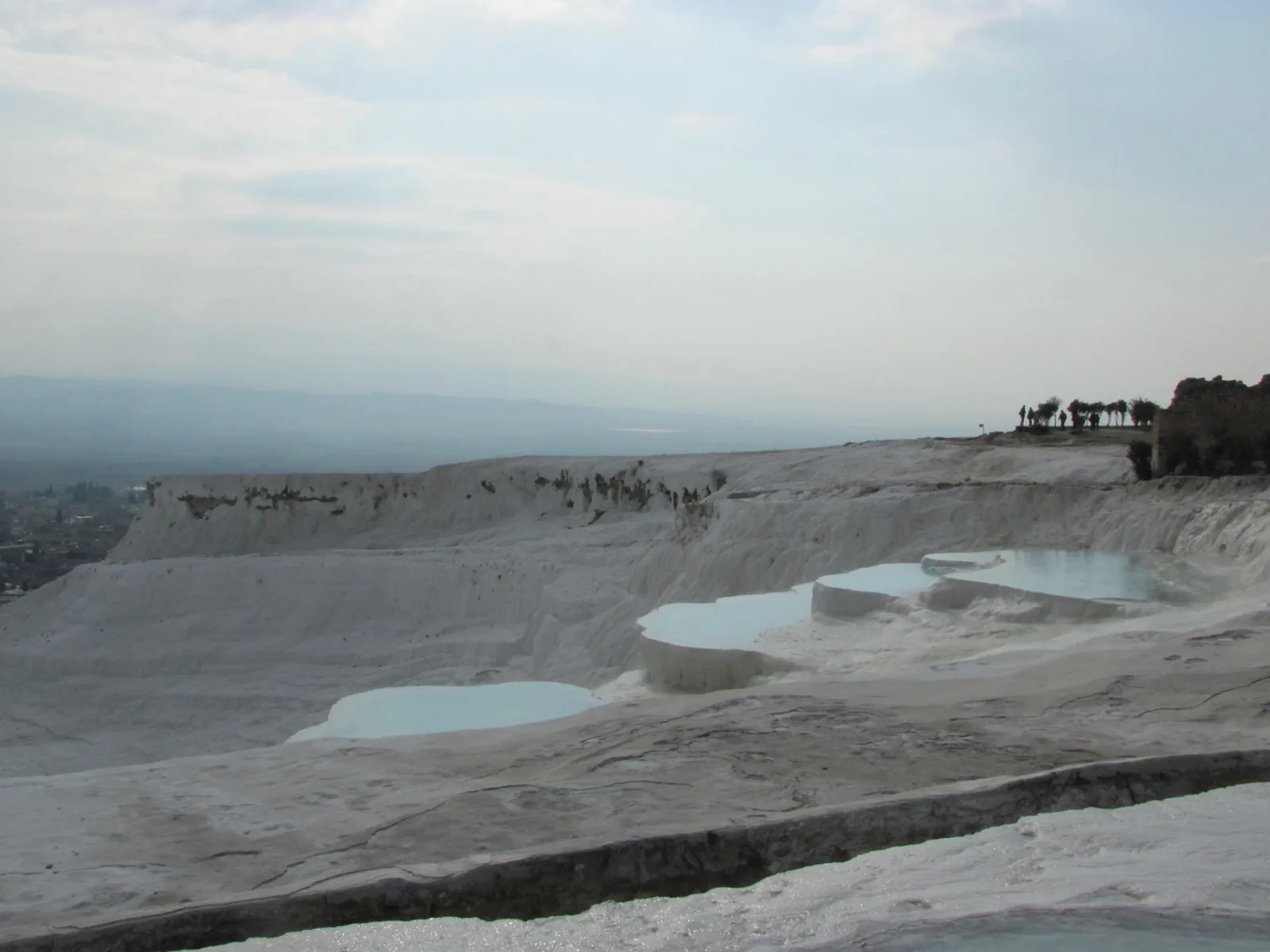 Pamukkale travertine terraces showing white mineral formations with small turquoise pools and visitors on the rim