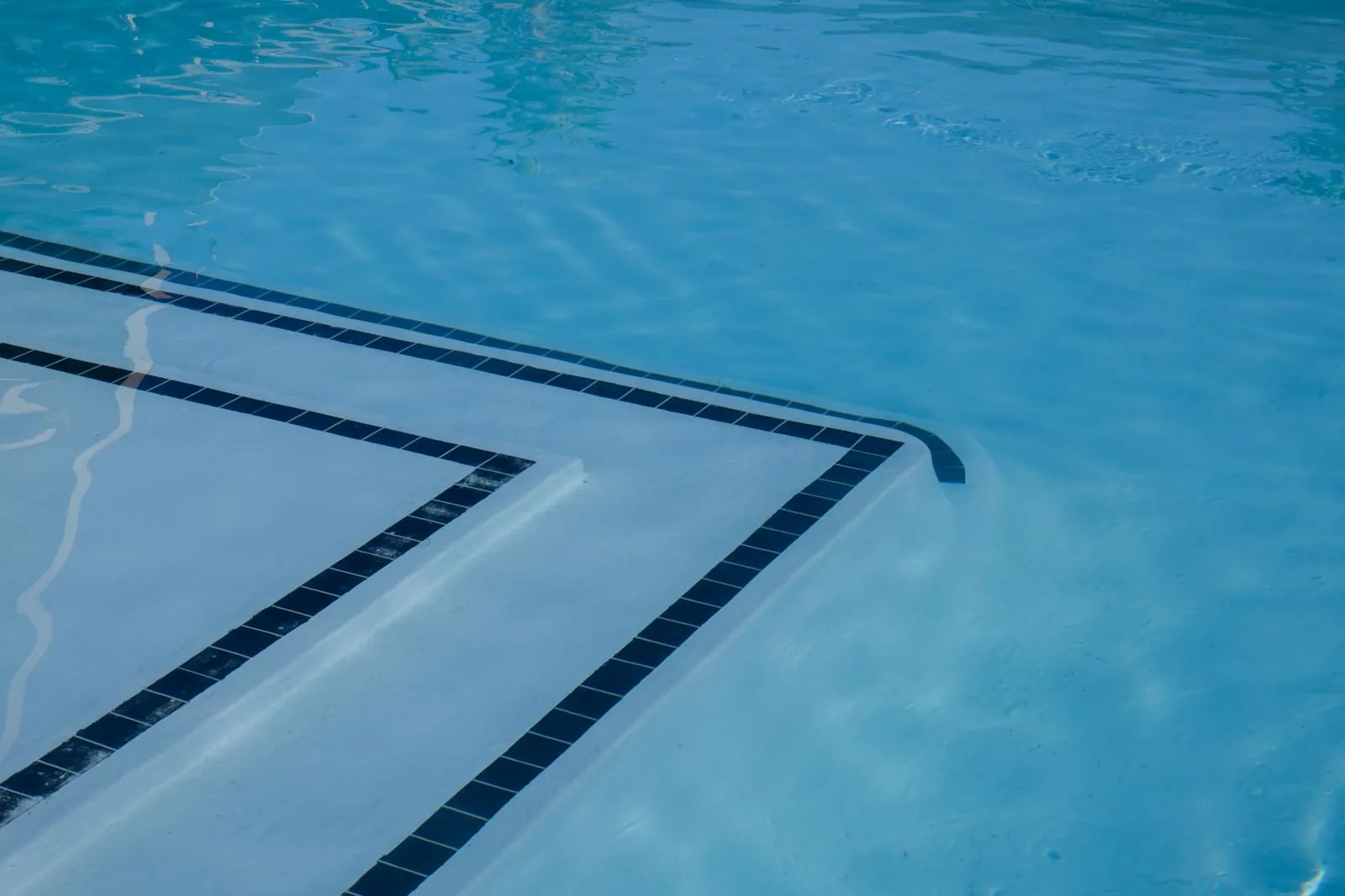 Crystal-clear blue swimming pool water showing the tiled entry steps with dark border tile trim through the water