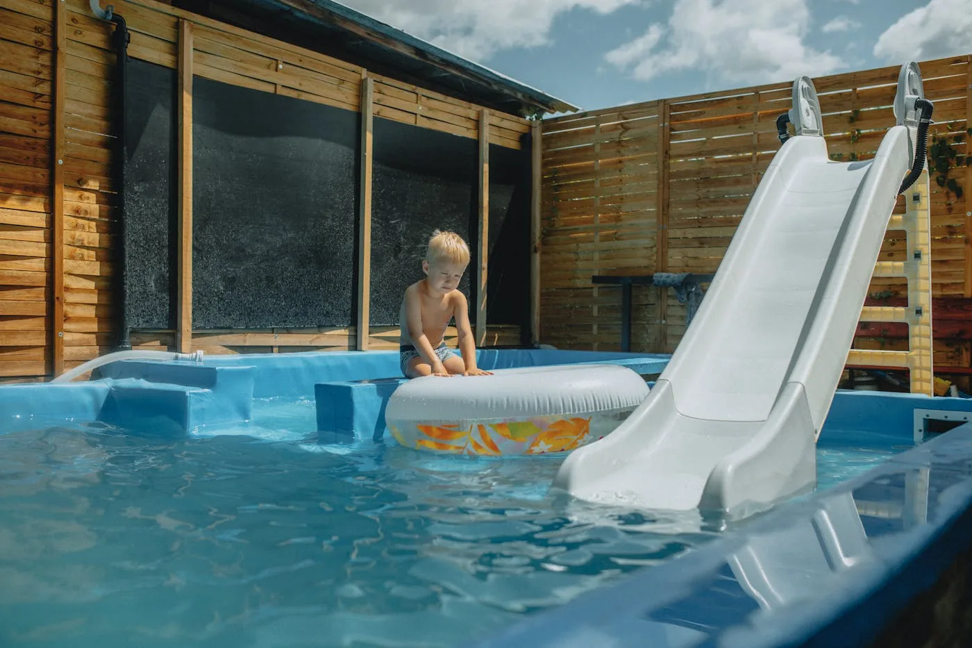 Child enjoying a rectangular above-ground pool with water slide in a fenced backyard garden