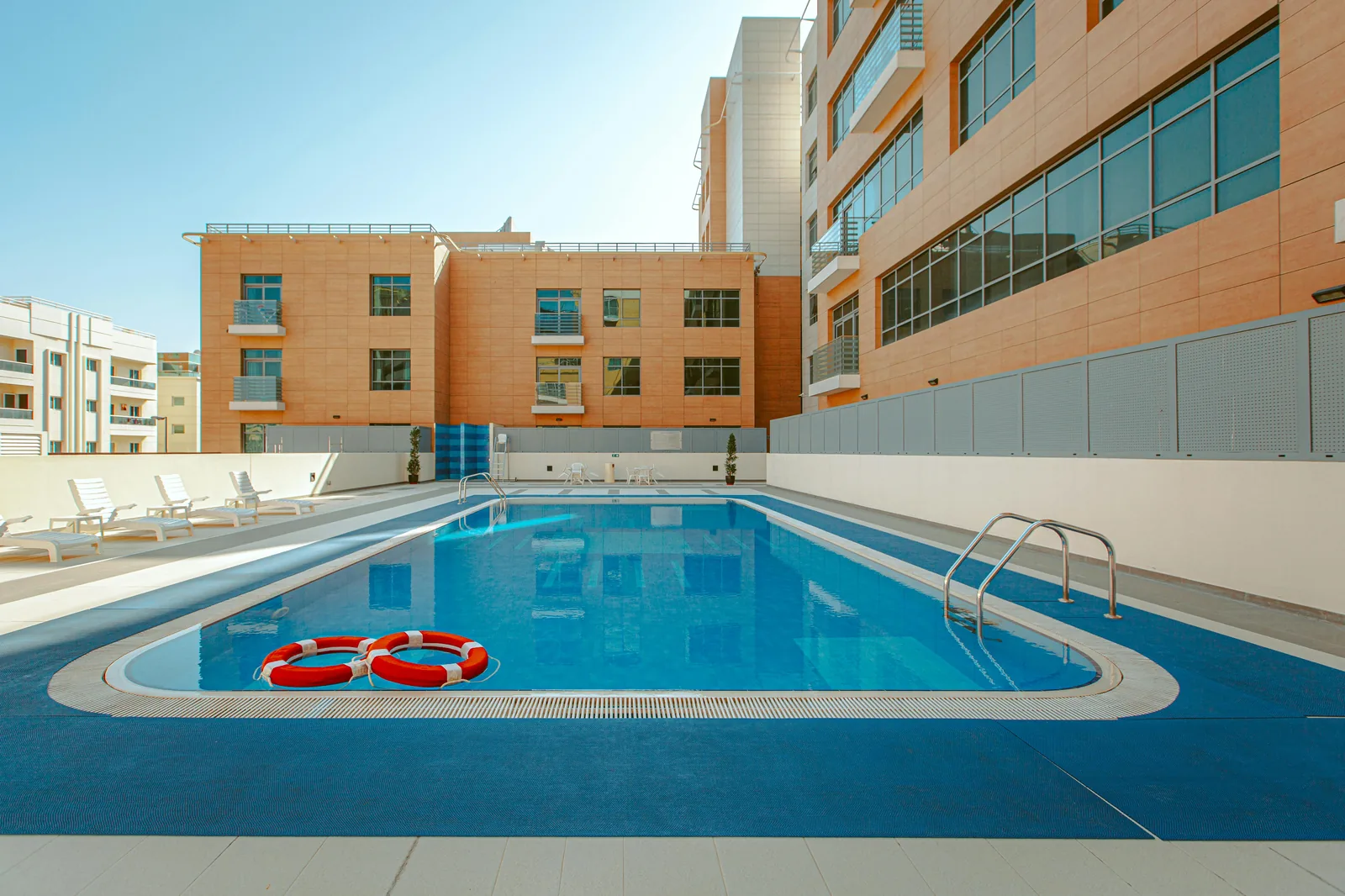 Clean outdoor swimming pool with safety ring beside a modern building