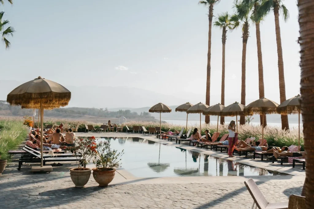 A luxury outdoor hotel swimming pool with sun loungers palm trees and straw umbrellas in a Mediterranean setting representing hotel pools in Seville Spain where temperatures reach 43 to 44 degrees Celsius in summer