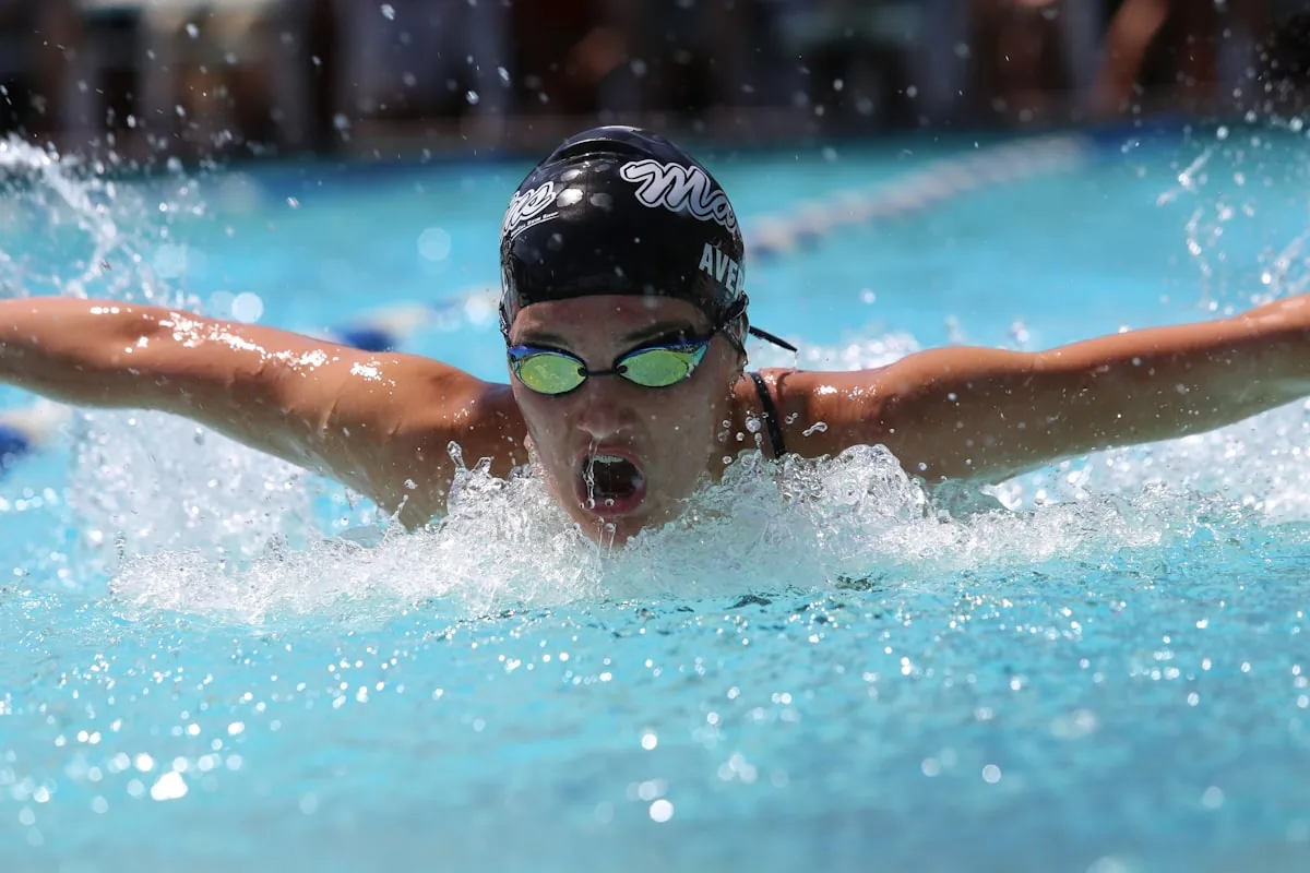 A female competitive swimmer performing butterfly stroke with goggles, representing the use of goggles as a practical prevention measure against pool chlorine eye irritation