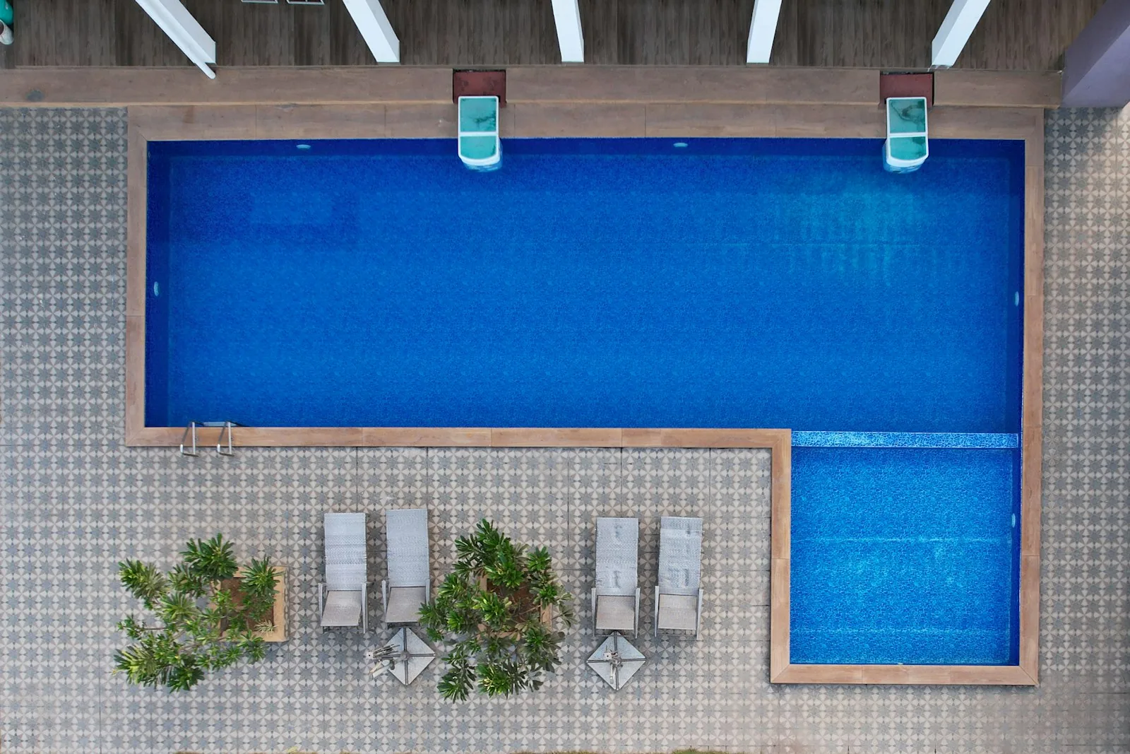 Aerial overhead view of a compact rectangular swimming pool with a separate spa section and sun loungers on a tiled poolside area