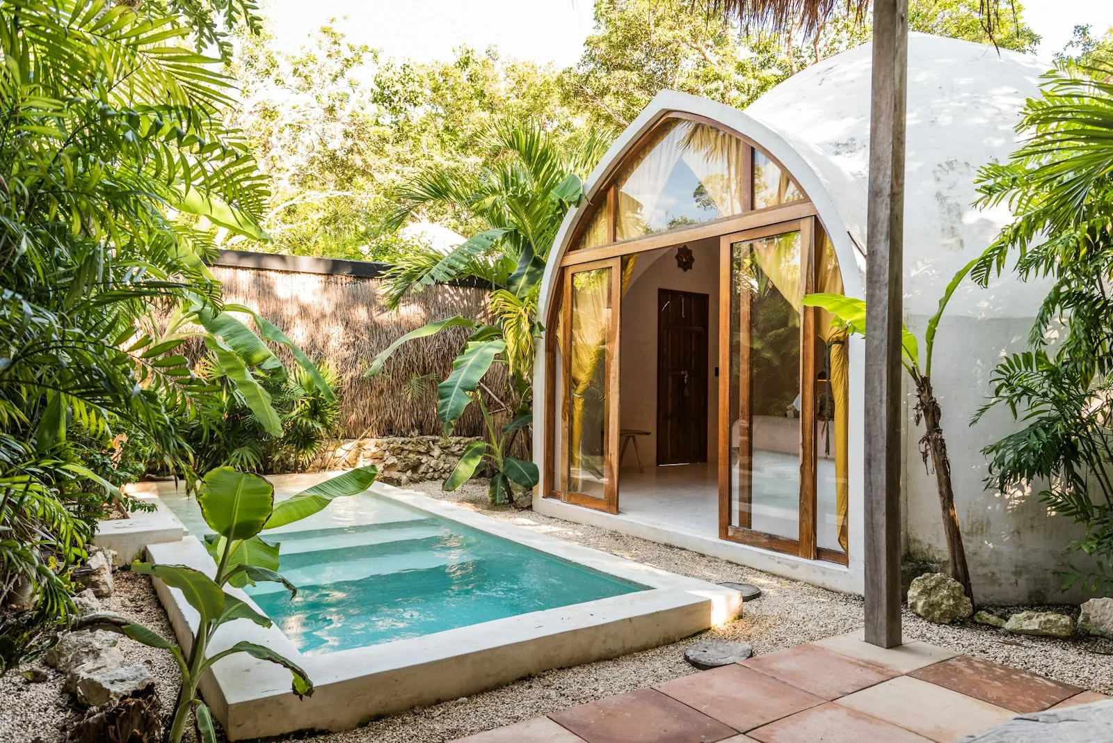 A small plunge pool set into a garden surrounded by lush tropical planting and a white villa building, representing compact pool options for residential gardens