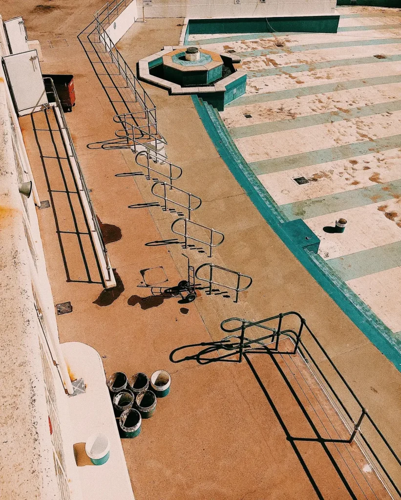 An empty outdoor concrete swimming pool with painted teal lane markings and paint buckets on the ground representing swimming pool paint application for concrete pools using chlorinated rubber or epoxy pool coating