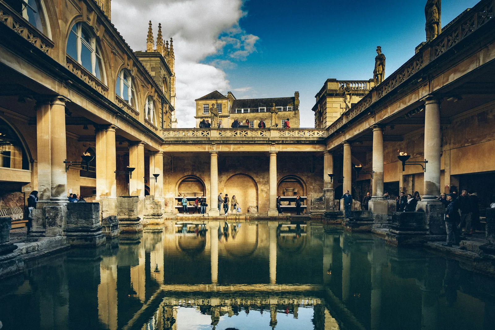 The historic Roman Baths in Bath UK with stone columns and a large pool reflecting the surrounding architecture