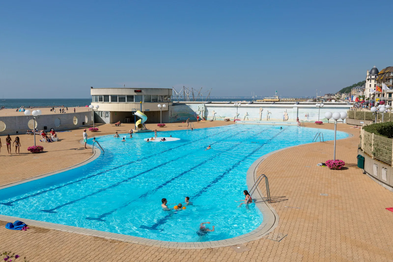 An outdoor lido or open-air swimming pool on a sunny summer day with swimmers and sunbathers