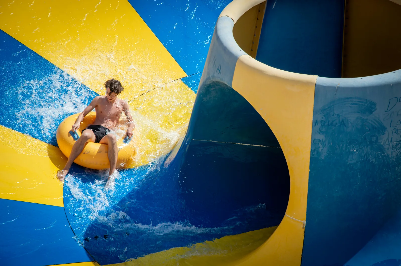 An indoor leisure centre swimming pool with a bright colourful water slide descending into a splash pool alongside a main pool with lane ropes representing UK leisure centre pools with flumes and slides