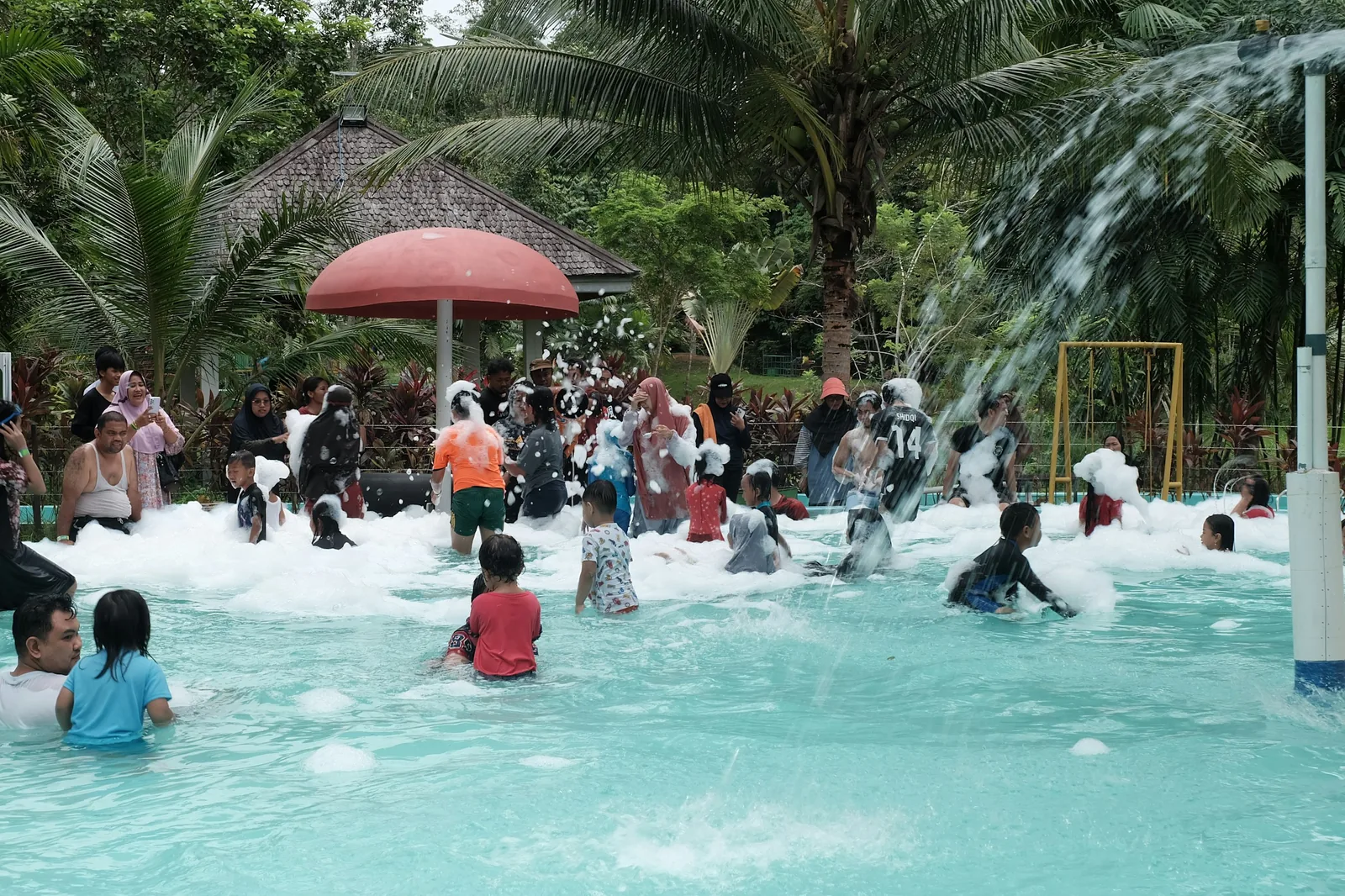 Families and children enjoying a busy leisure pool with foam water jets and interactive water features, representing family swimming pool sessions at Glasgow and nearby leisure centre facilities