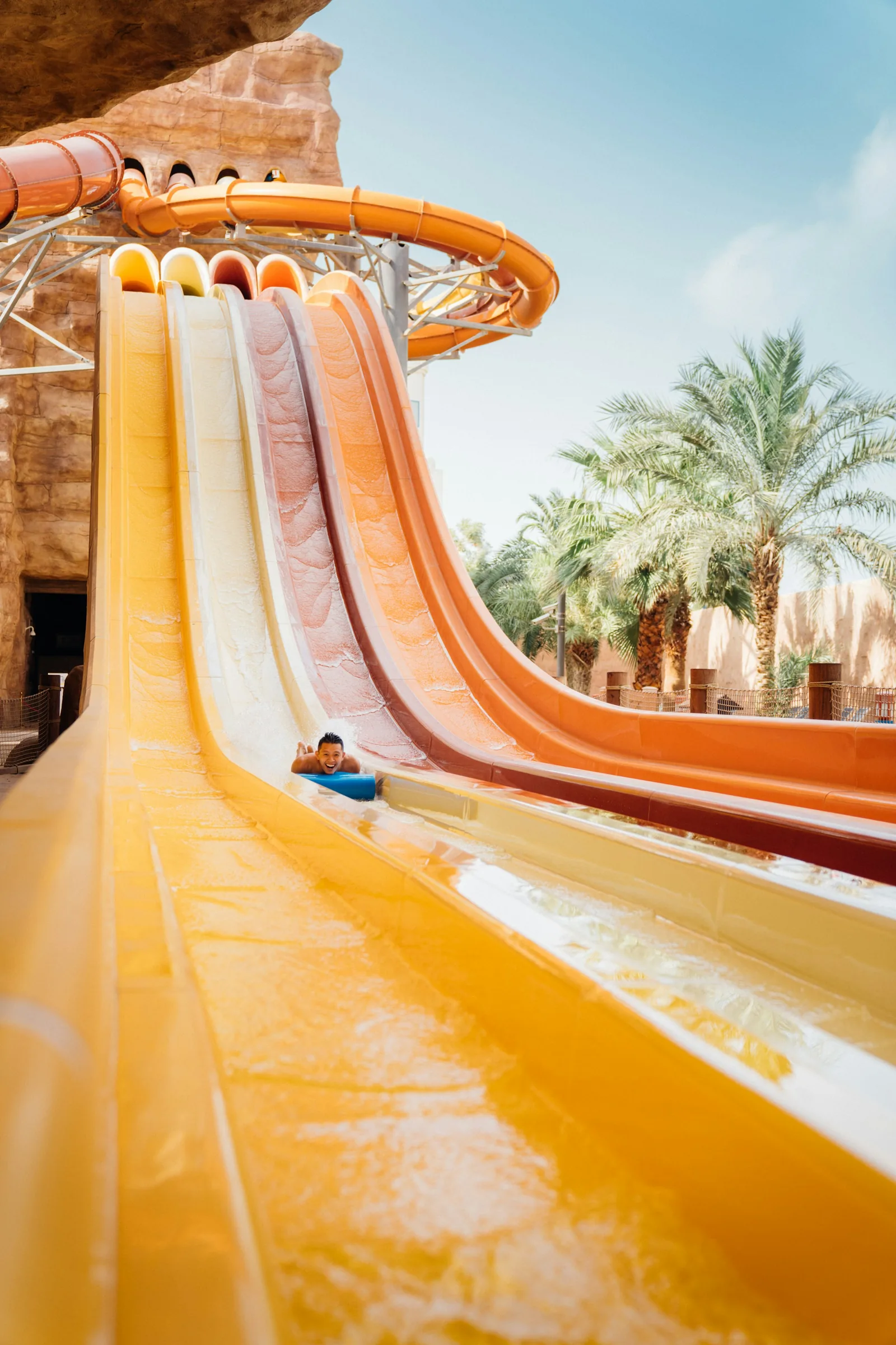 A person riding down a yellow racing water flume slide at a water park with multiple parallel slides, representing the flume rides available at Hamilton Water Palace, The Time Capsule, and ON-X near Glasgow