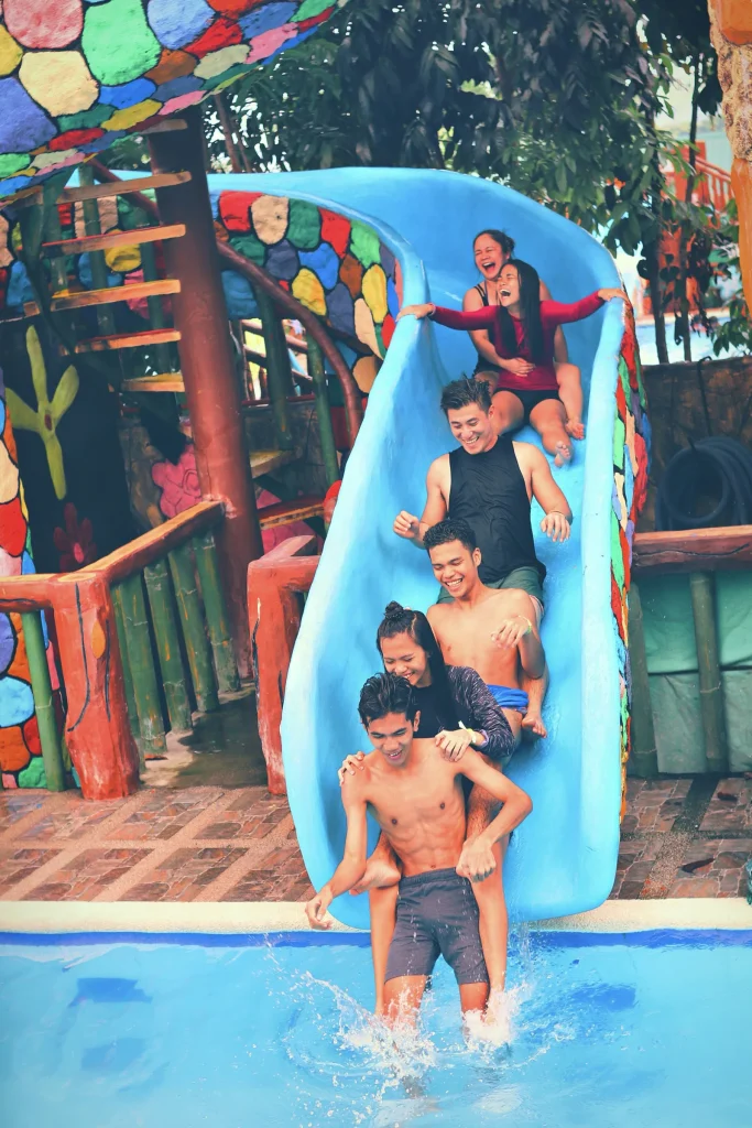A group of people laughing and smiling together on a blue water slide at an outdoor leisure pool, representing the fun pool and slide facilities at Glasgow and nearby leisure centres