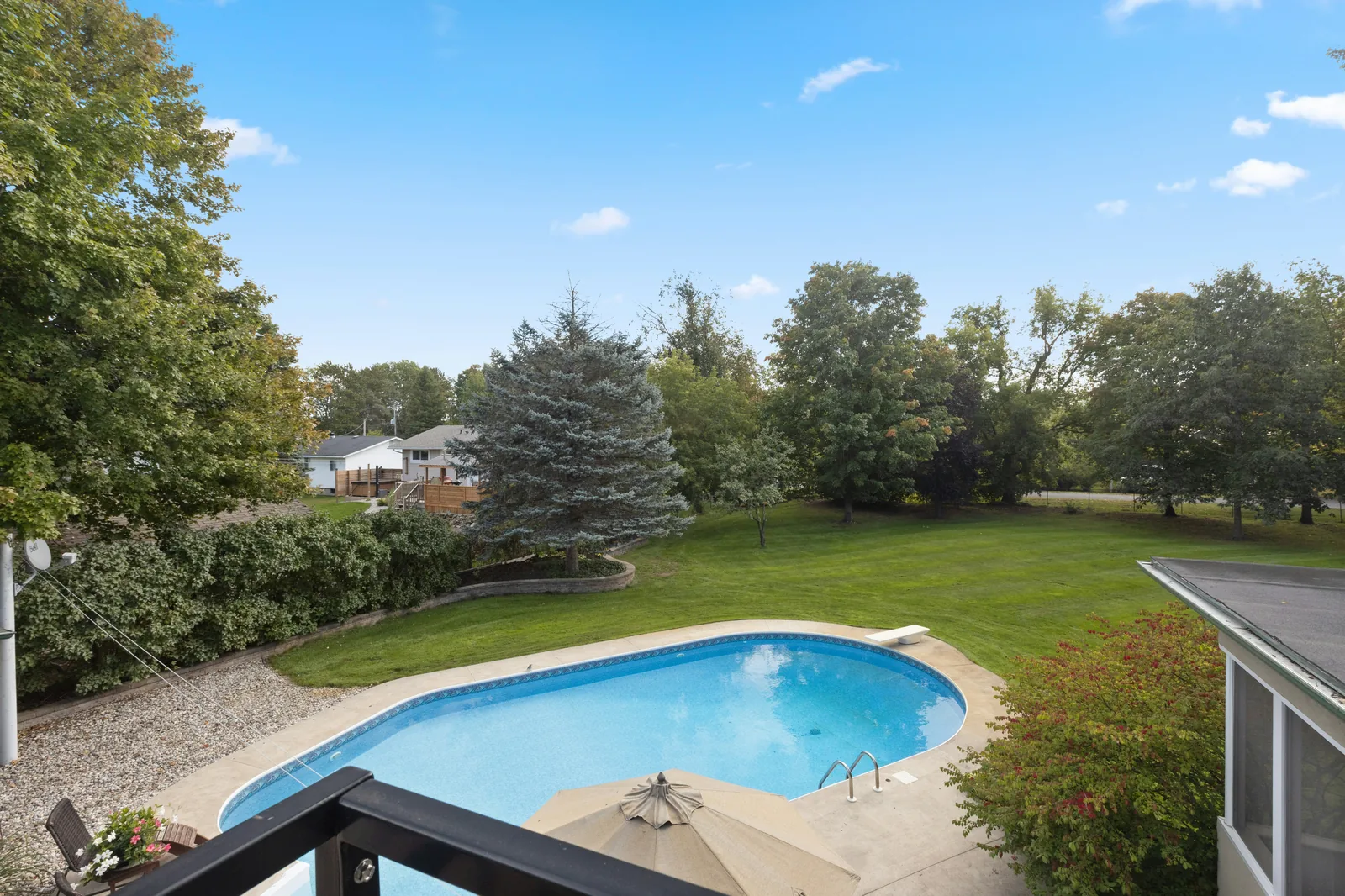 Kidney-shaped in-ground swimming pool in a large garden with lawn and mature trees