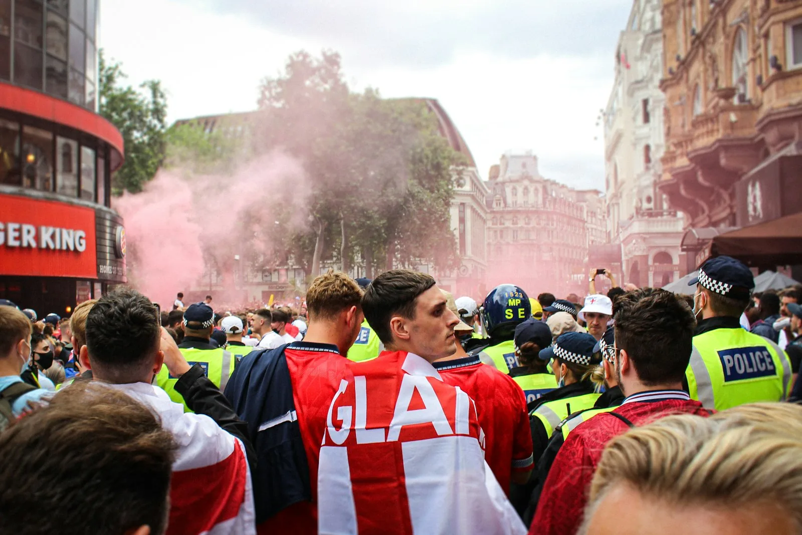 England football fans in red and white jerseys on London streets with coloured smoke, representing the mass participation in British football culture that underpinned the Littlewoods football pools industry in the 1960s
